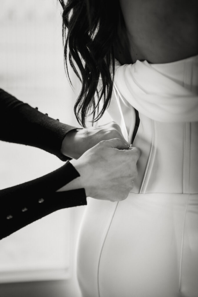 Hochzeitsfotografie Starnberg. Das Foto zeigt eine Detailaufnahme eines Brautkleides, welches gerade geschlossen wird.